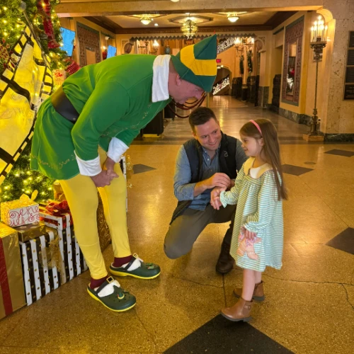 Travis and an dressed up elf with young girl in front of Christmas tree