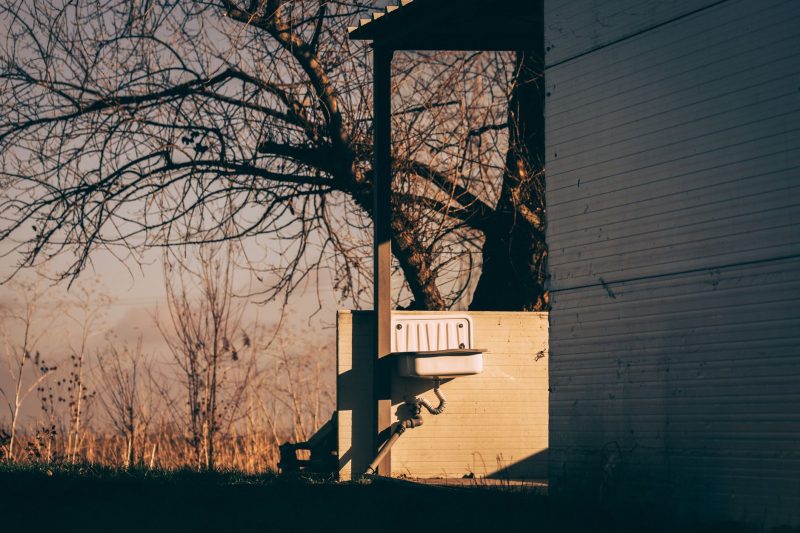 Abandoned outdoor sink beside a bare tree, illuminated by soft autumn light.