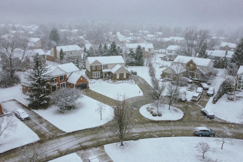 Aerial view of a snow-covered suburban neighborhood with quiet streets and frosted rooftops.